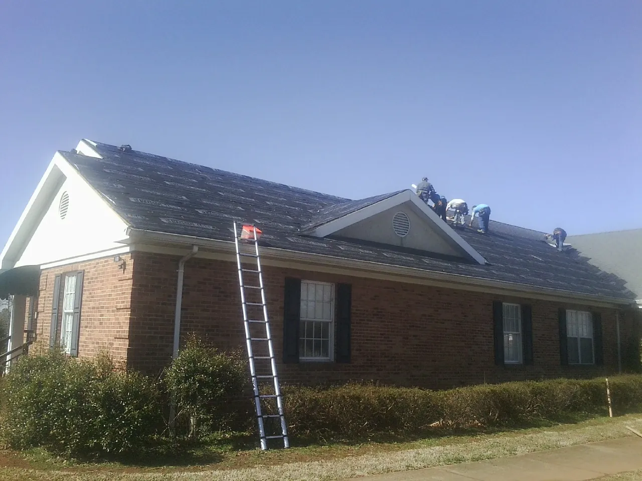 Crew tearing shingles off a brick ranch roof with a ladder set — Emergency Roof Repair work by our crew in Doyle
