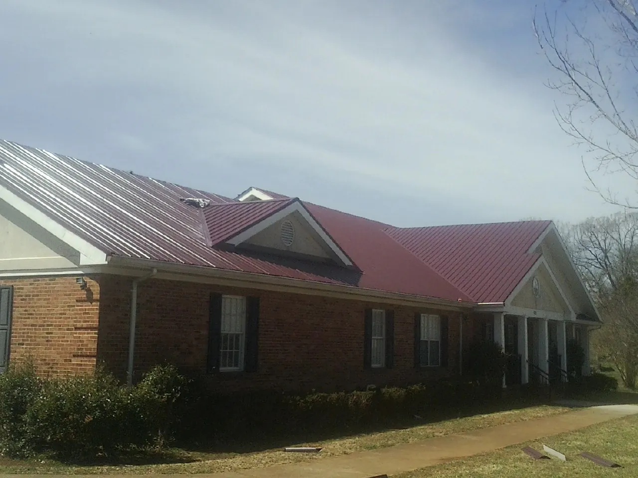 Red metal roof with gabled entries on a long brick building, from a Hail Damage Roof Repair job in Doyle