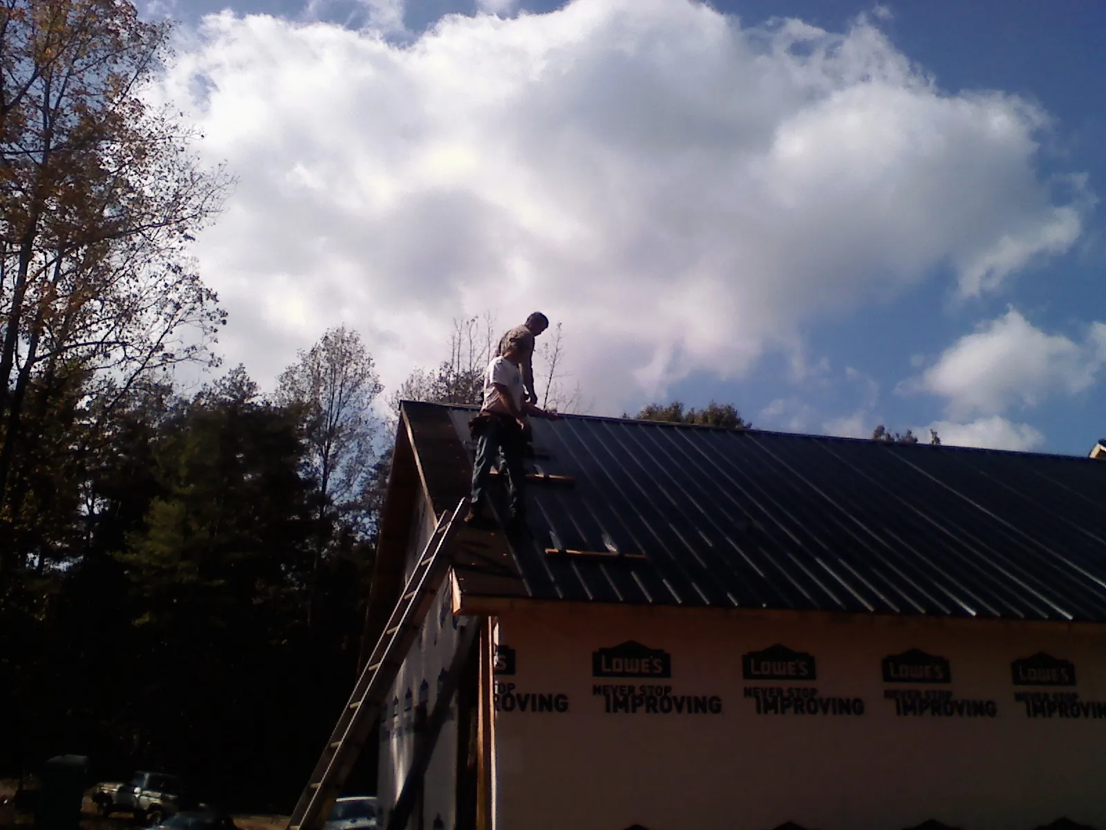 Roofer fastening dark metal panels high against a cloudy sky, from a Roof Inspection job in Doyle