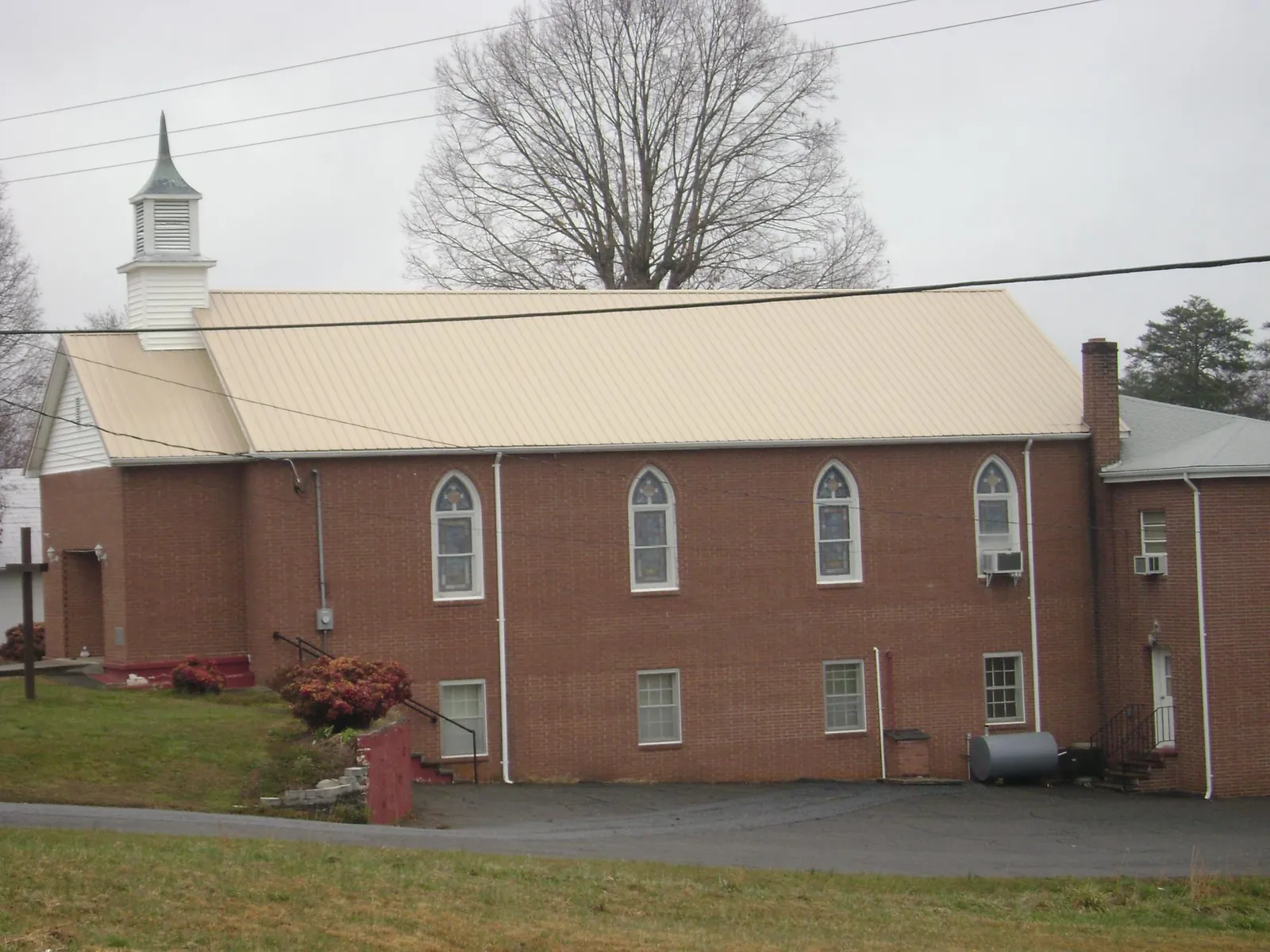 New tan metal roof on a brick church with a white steeple in Doyle