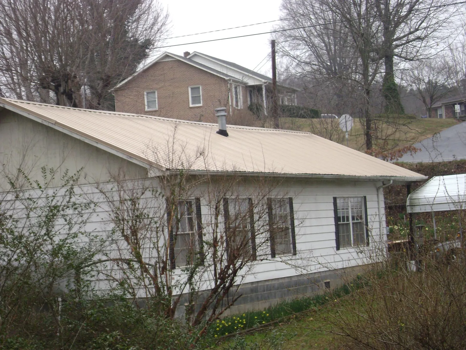 Tan metal roof on a white sided house set into a hillside — Commercial Roofing by Roofing Brothers in Doyle